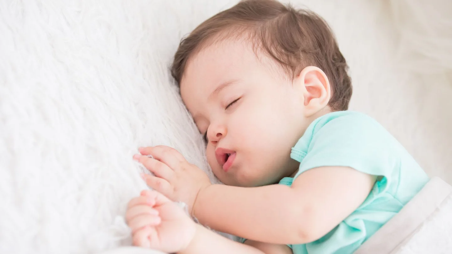 Бебе, облечено в светлозелена пижама, спи спокойно на бяла мека постелка. Консултации за сън за бебета и деца с индивидуален подход.