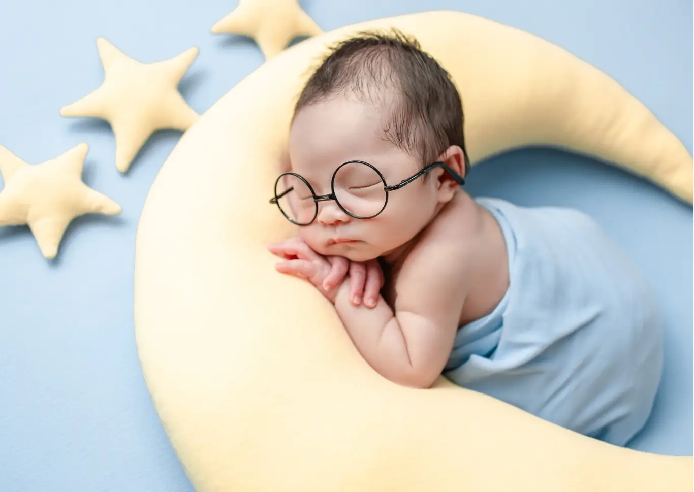 Бебе със смешни очила спи върху жълта плюшена луна, обгърнато в син плат. Консултации за правилното разбиране и прилагане на методите за самостоятелно заспиване, без оставяне на бебето да плаче.