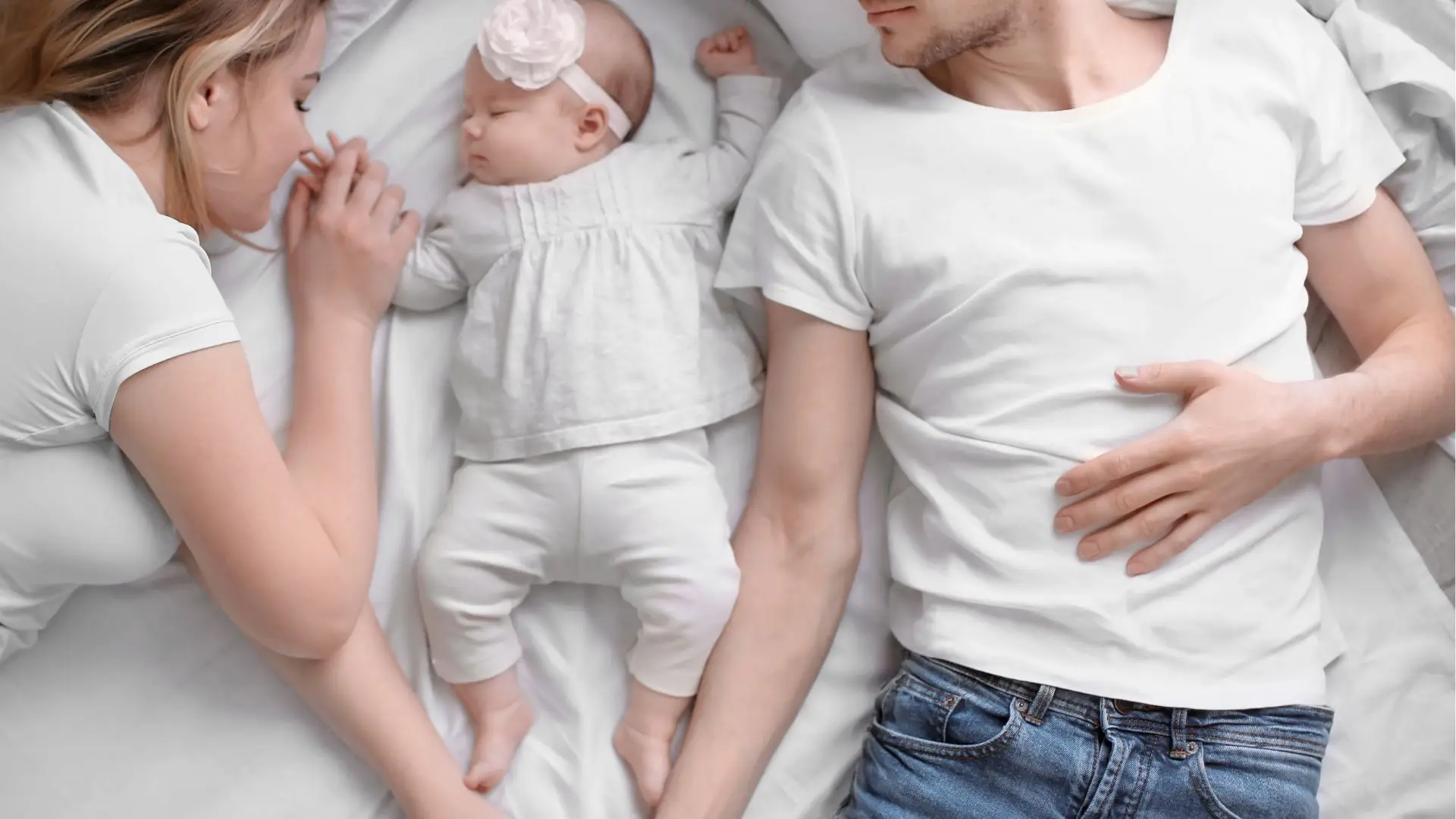 Майка и баща лежат в леглото със спящо бебе помежду им. Всички са облечени в бели дрехи и се държат за ръце. Консултациите предлагат индивидуален подход за нуждите на бебето и семейството.